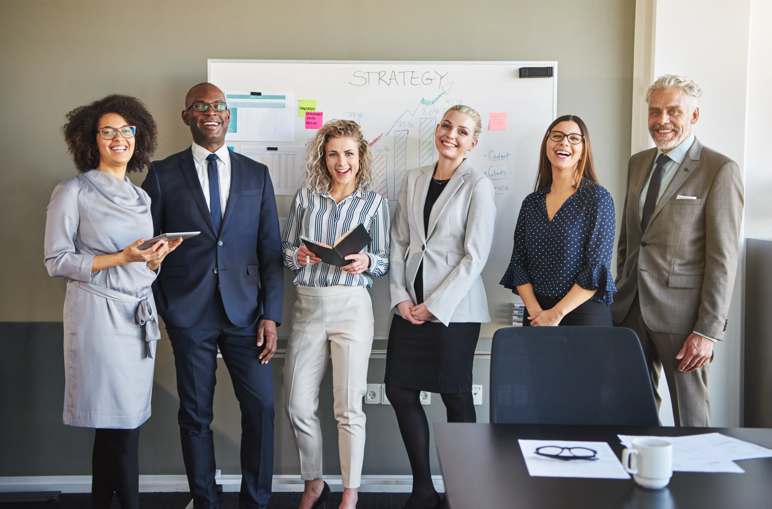 team-of-business-people-looking-at-camera-2024-09-18-11-25-27-utc Business people of men and women standing and smiling in front of white board with various notes on it